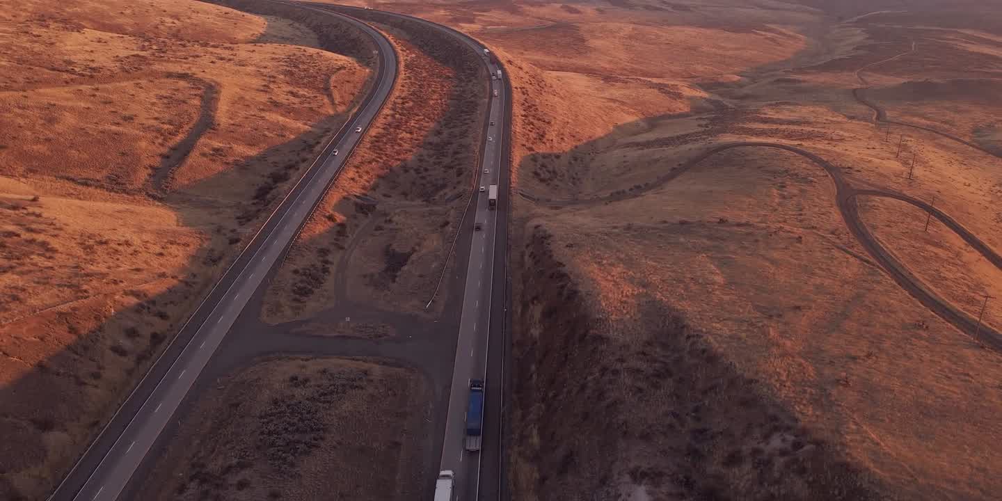 Motorväg i kvällssol genom gyllene kullar, lastbilar på väg